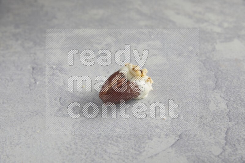 Pecan stuffed date covered with white chocolate and chopped walnuts on alight grey background