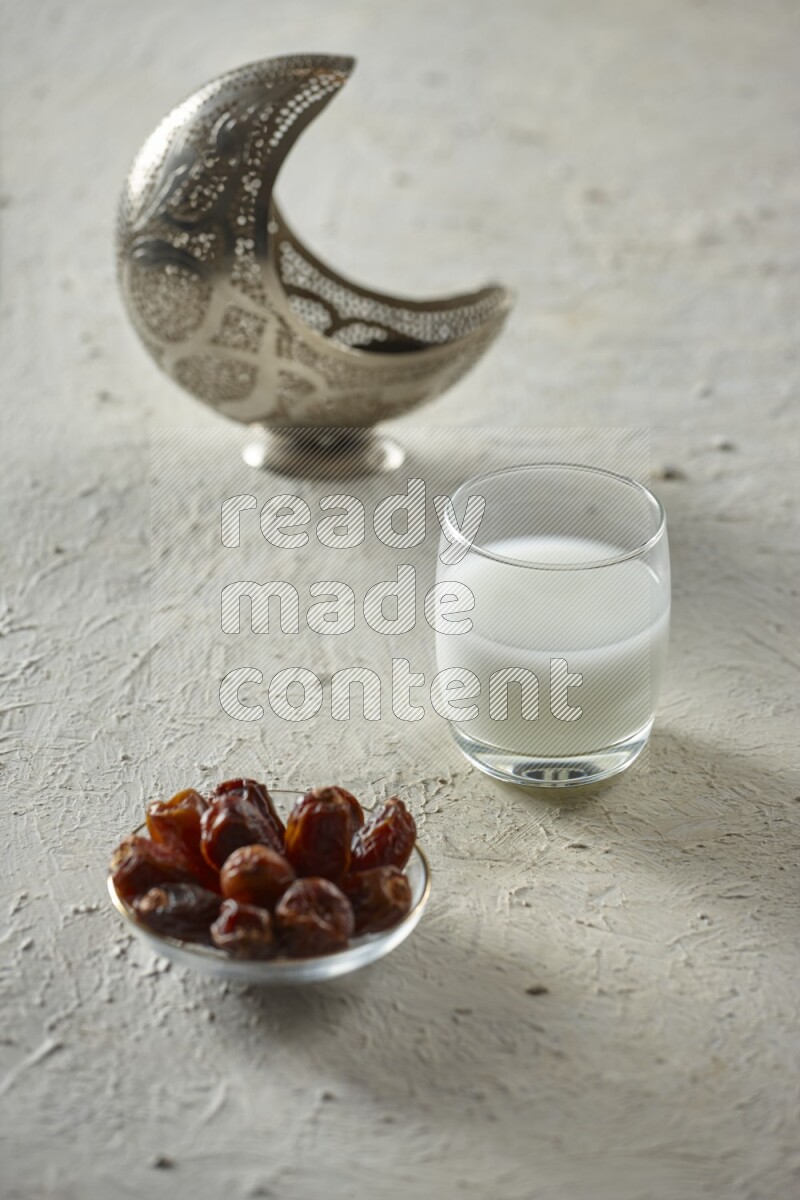 A silver lantern with different drinks, dates, nuts, prayer beads and quran on textured white background