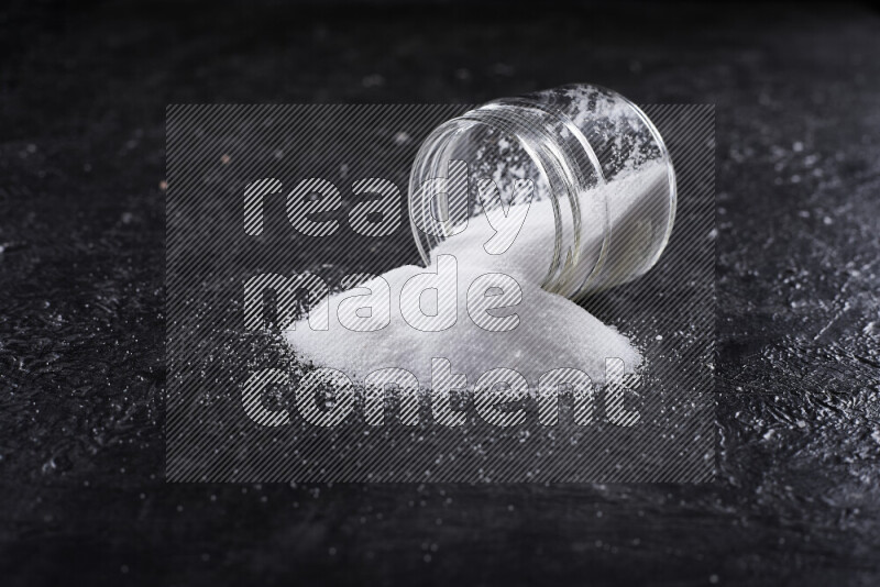 A glass jar full of fine table salt on black background