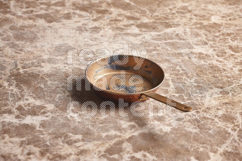 A small copper pan on beige marble background