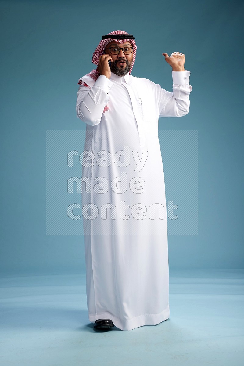 Saudi Man with shimag Standing talking on phone on blue background