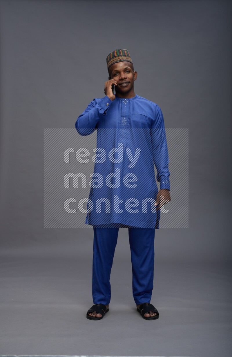 Man wearing Nigerian outfit standing talking on phone on gray background