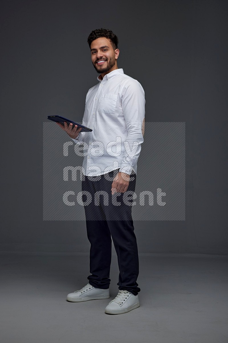 A man wearing smart casual standing and using his tablet eye level on a gray background