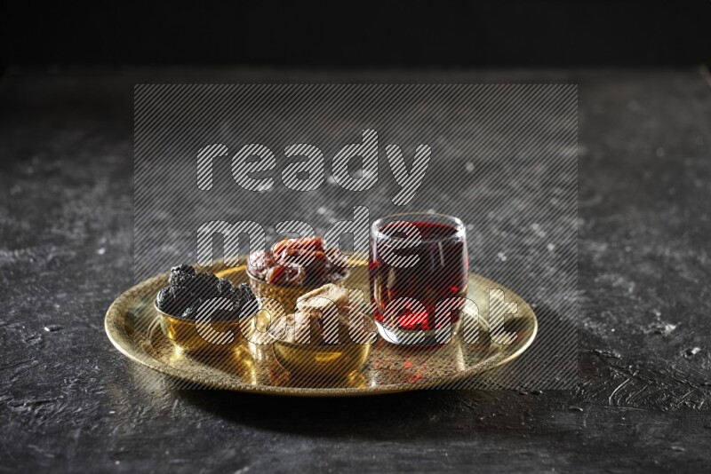 Dried fruits in metal bowls with Hibiscus on a tray in dark setup