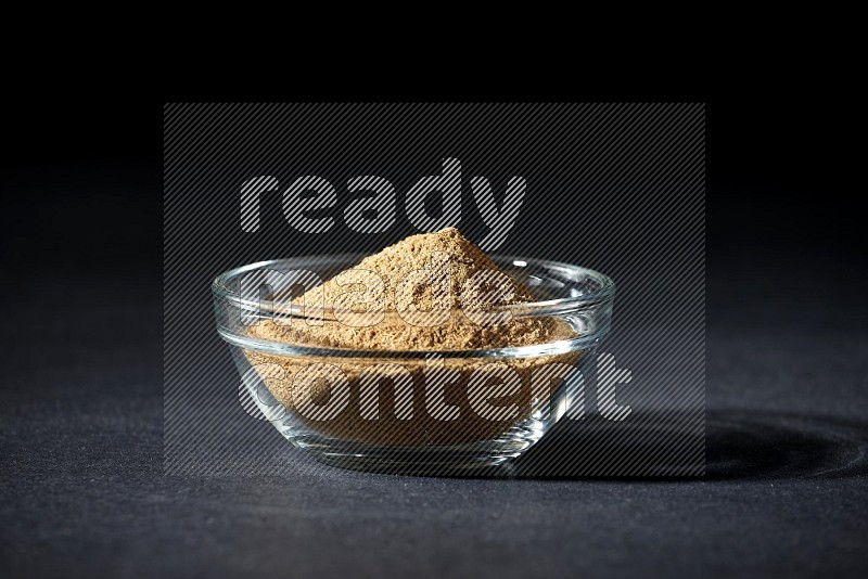 A glass bowl full of cumin powder on black flooring