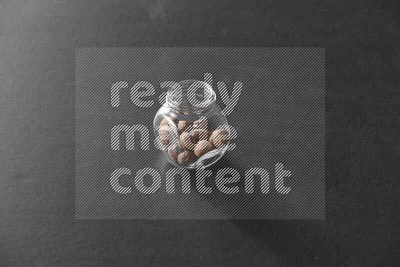 A glass spice jar full of nutmeg on black flooring