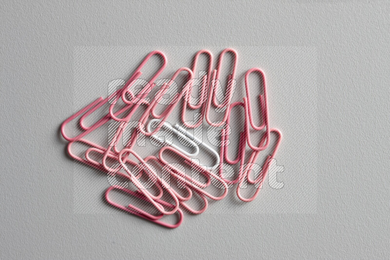 مجموعة من مشابك الورق الوردية مع مشبك ورق ملون مختلف في المنتصف على خلفية رمادية