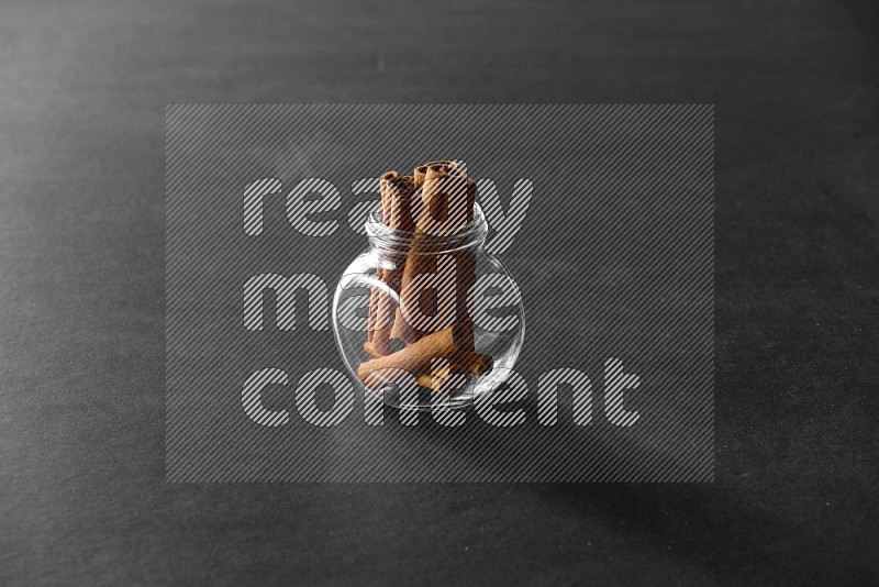 A glass spice jar full of cinnamon sticks on black flooring