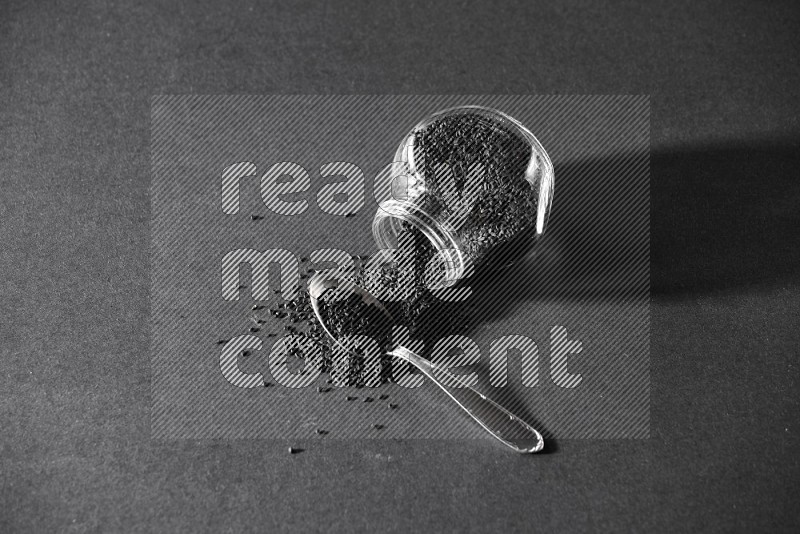 A glass spice jar full of black seeds flipped and seeds spread out with a metal spoon full of the seeds on a black flooring in different angles