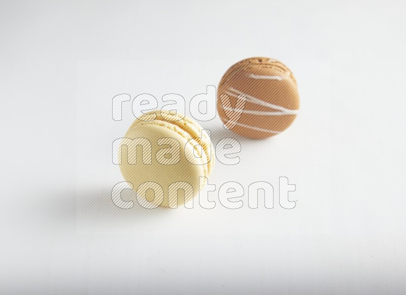 45º Shot of of two assorted Brown Irish Cream, and Yellow Vanilla macarons on white background