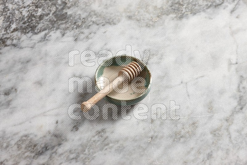 Multicolored Pottery bowl with wooden honey handle in it, on grey marble flooring, 65 degree angle