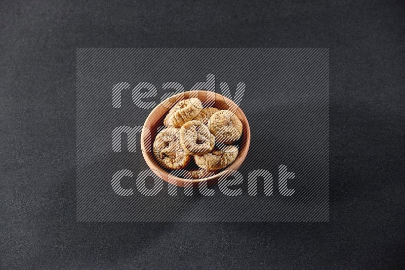 A wooden bowl full of dried figs on a black background in different angles