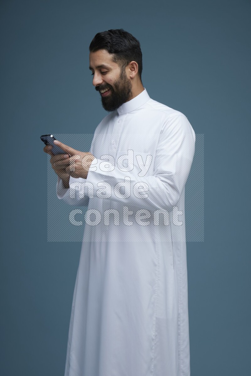 A man Texting in a blue background wearing Saudi Thob