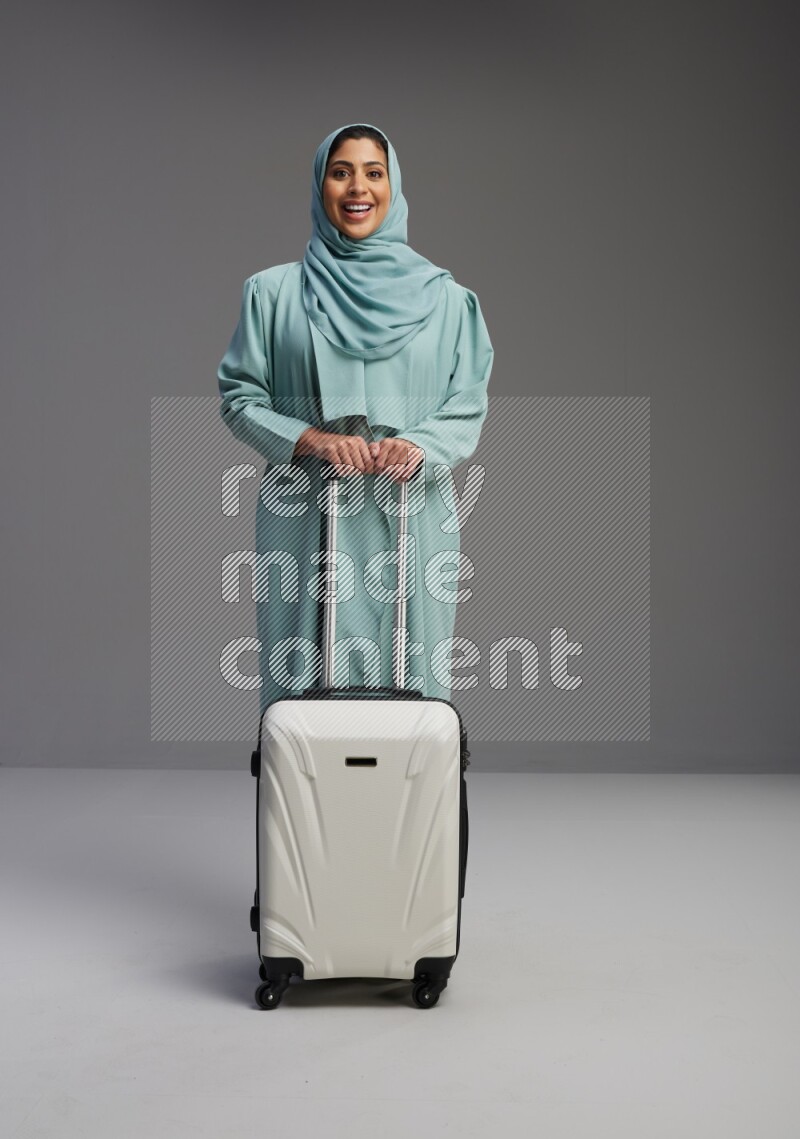 Saudi Woman wearing Abaya standing holding Travel bag on Gray background