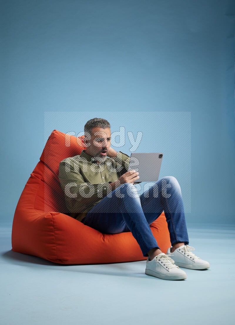 A man sitting on an orange beanbag and working on tablet