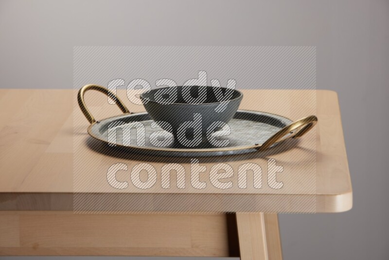 grey bowl placed on a rounded stainless steel tray with golden handels on the edge of wooden table