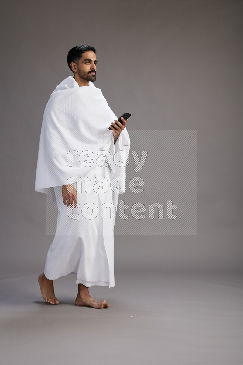 A man wearing Ehram Standing texting on phone on gray background