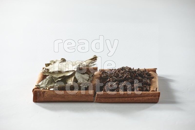 مربعان من أعواد القرفة ممتلئان بالقرنفل وأوراق الغار علي خلفية بيضاء