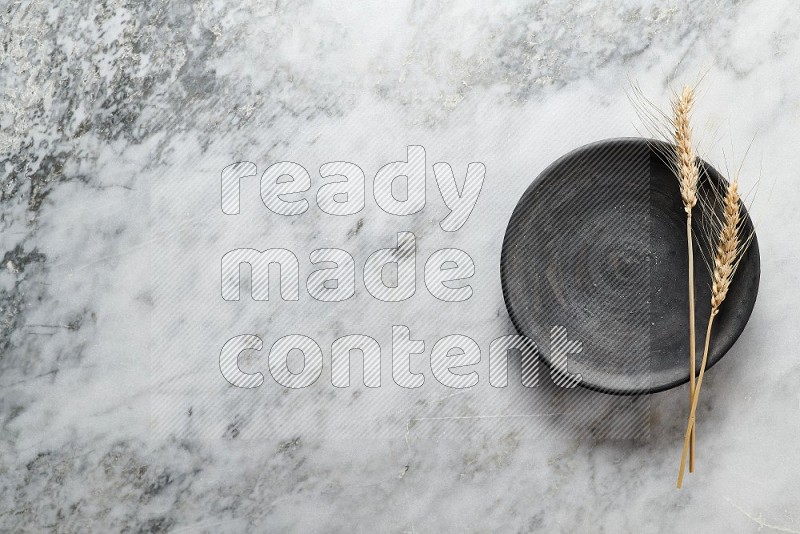 Wheat stalks on Black Pottery Plate on grey marble flooring, Top view