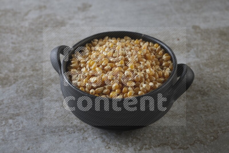corn kernel in a black handheld ceramic bowl on a grey textured countertop