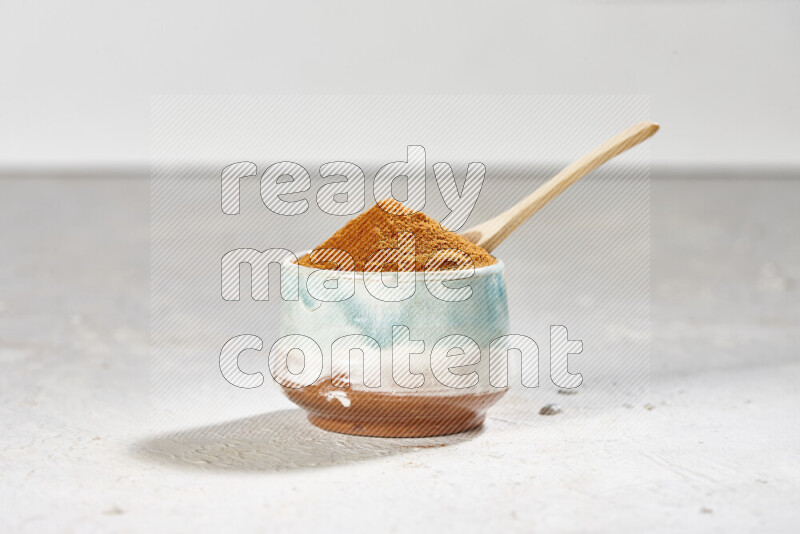 A colored pottery bowl full of ground paprika powder on white background