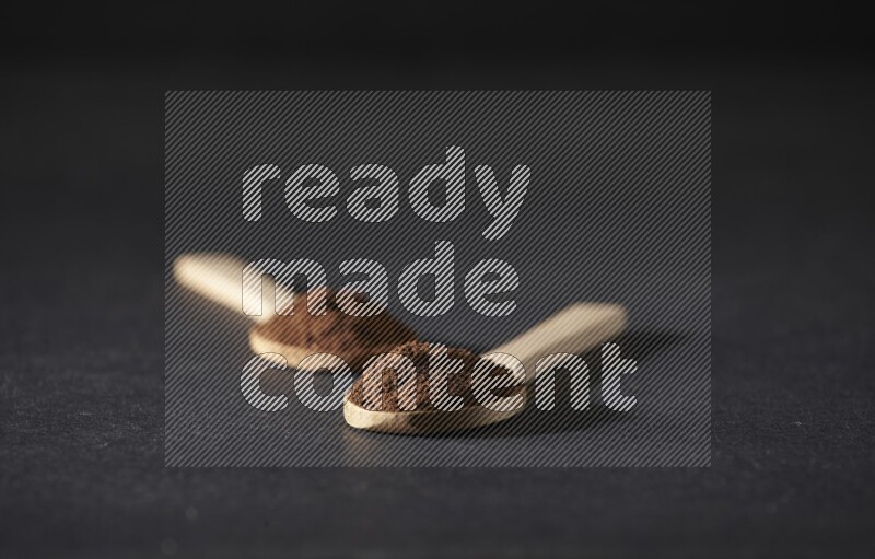 2 wooden spoons full of cloves powder on a black flooring