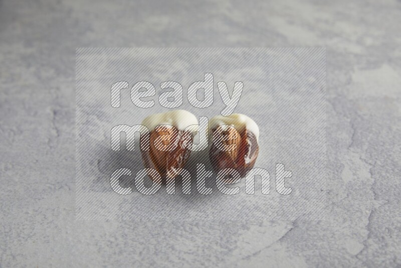 two almonds stuffed dates covered with white chololate on a light grey background