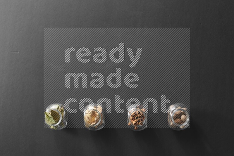 أوراق الغار وزنجبيل مجفف وقرفة وجوزة الطيب في أوعية زجاجية علي خلفية سوداء