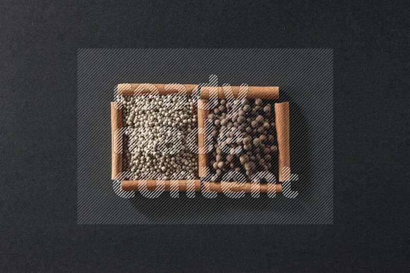 مربعان من أعواد القرفة ممتلئان بحبوب الفلفل الأبيض وحبوب الفلفل الحلو علي خلفية سوداء