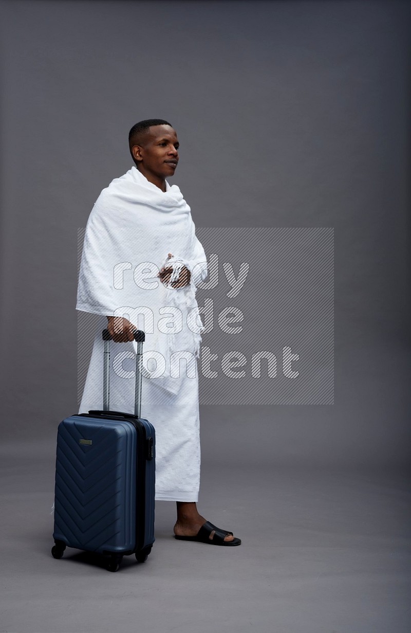 A man wearing Ehram Standing holding traveling bag on gray background