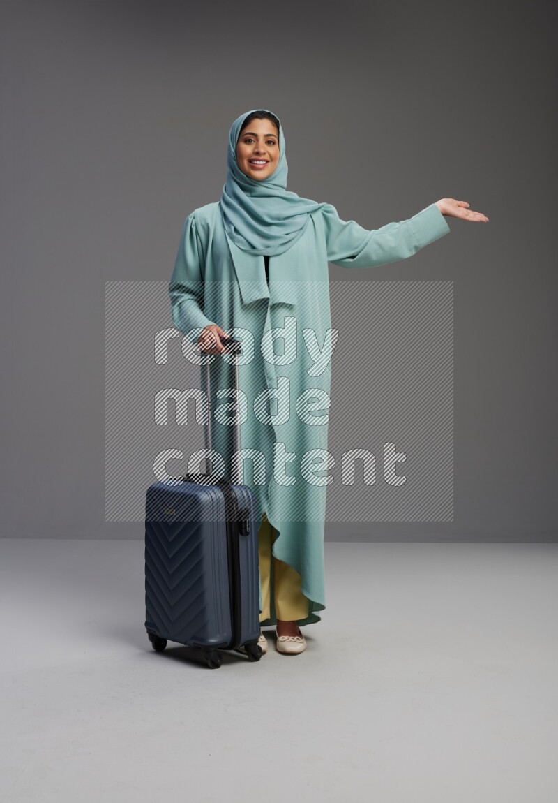 Saudi Woman wearing Abaya standing holding Travel bag on Gray background