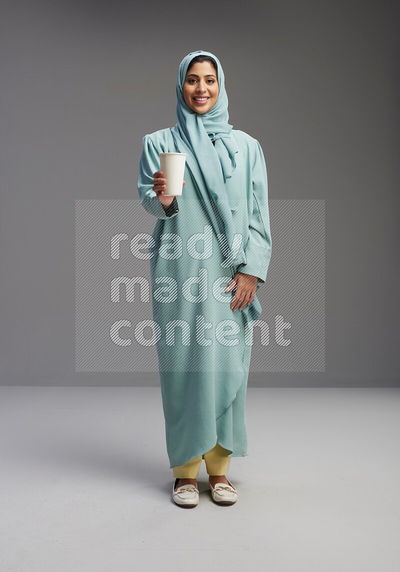 Saudi Woman wearing Abaya standing  holding paper cup on Gray background