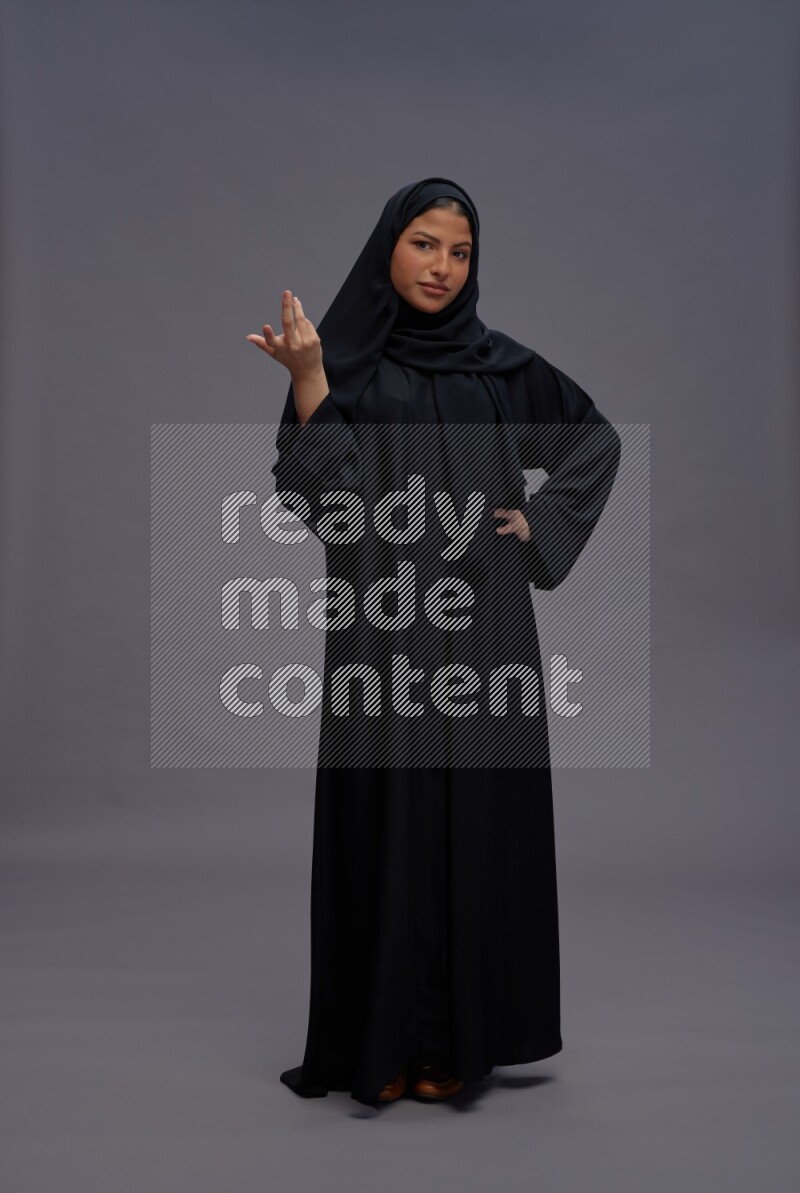 Saudi woman wearing Abaya standing interacting with the camera on gray background