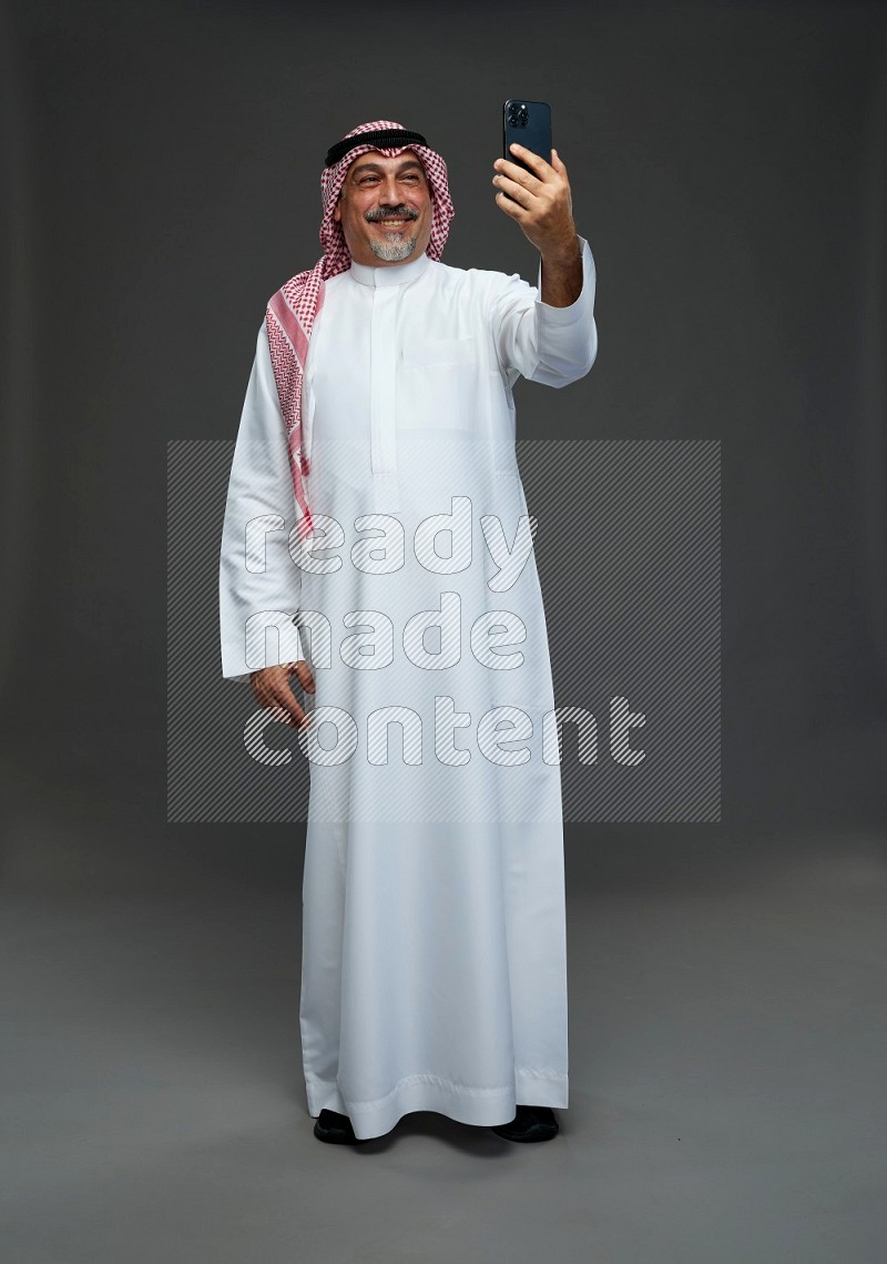 Saudi man with shomag Standing taking selfie on gray background