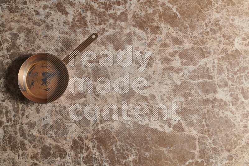A small copper pan on beige marble background