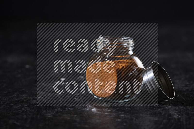 A glass jar full of ground paprika powder on black background