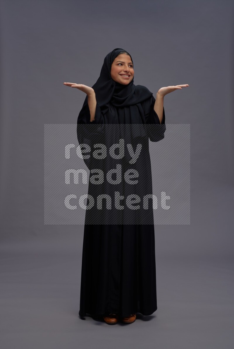 Saudi woman wearing Abaya standing interacting with the camera on gray background