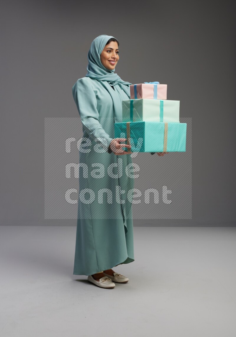 Saudi Woman wearing Abaya standing holding gift box on Gray background