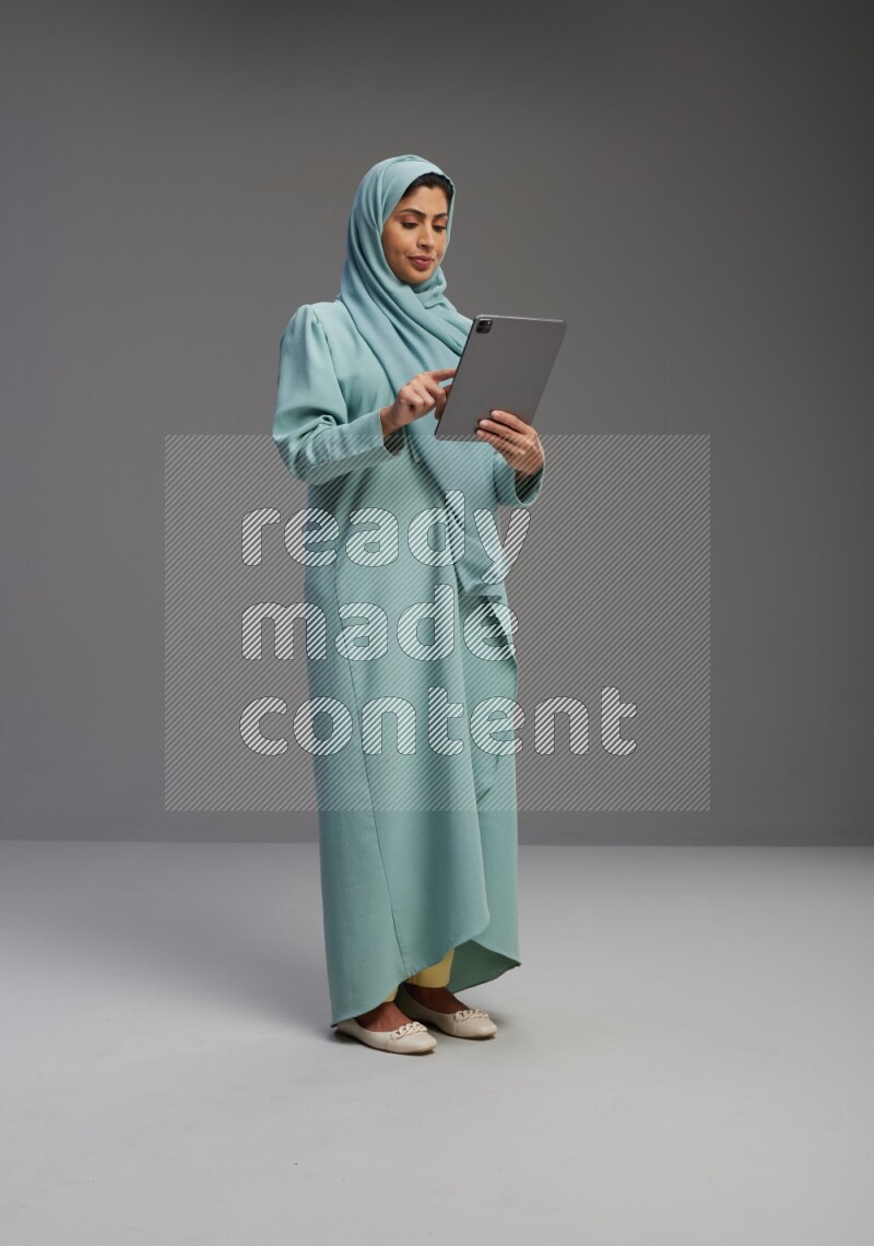Saudi Woman wearing Abaya standing working on tablet on Gray background