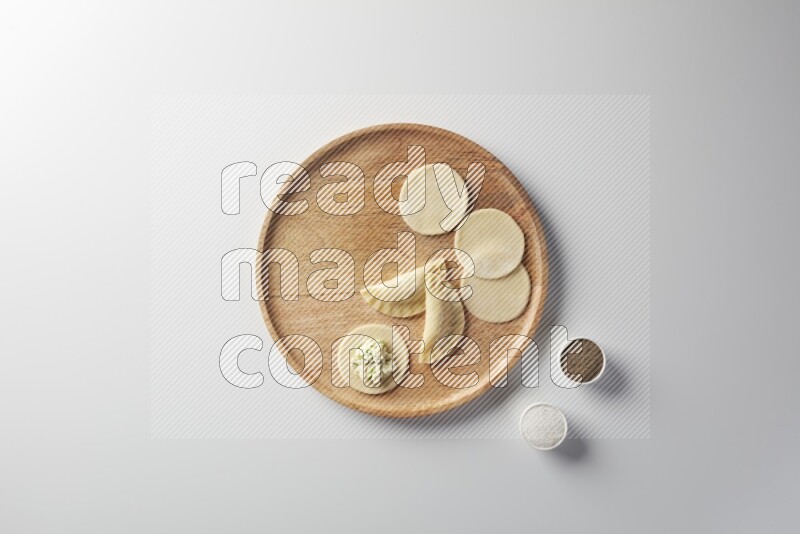 two closed sambosas and one open sambosa filled with cheese while salt, and black pepper aside in a wooden dish on a white background