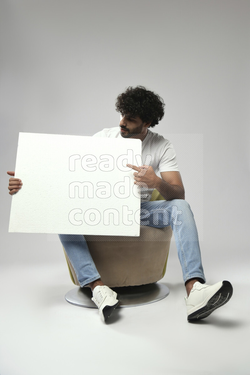 A man wearing casual sitting on a chair holding a white board on white background