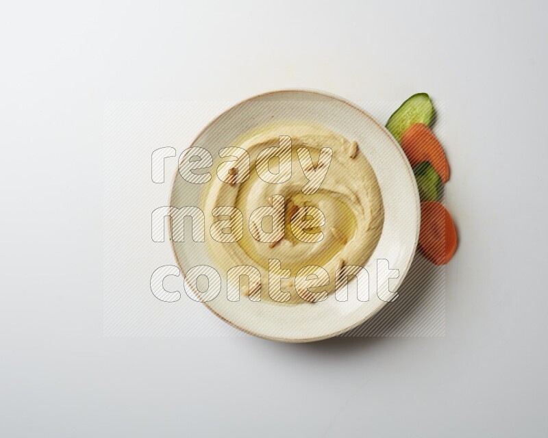 Hummus in a pottry plate garnished with pine nuts on a white background
