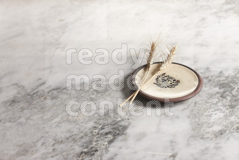 Wheat stalks on decorative pottery plate on grey marble background
