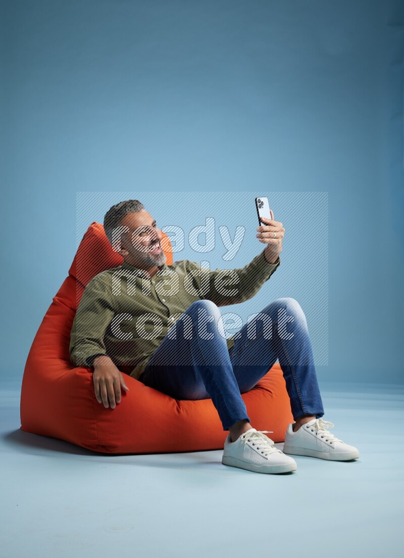 A man sitting on an orange beanbag and taking selfie