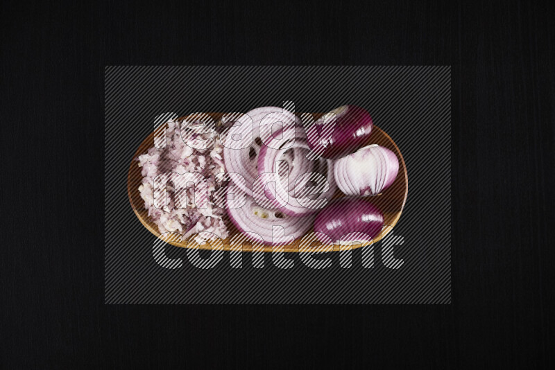 A close-up shot of red onions displayed in different forms including whole, sliced into rings, and finely chopped arranged on a wooden plate on black background