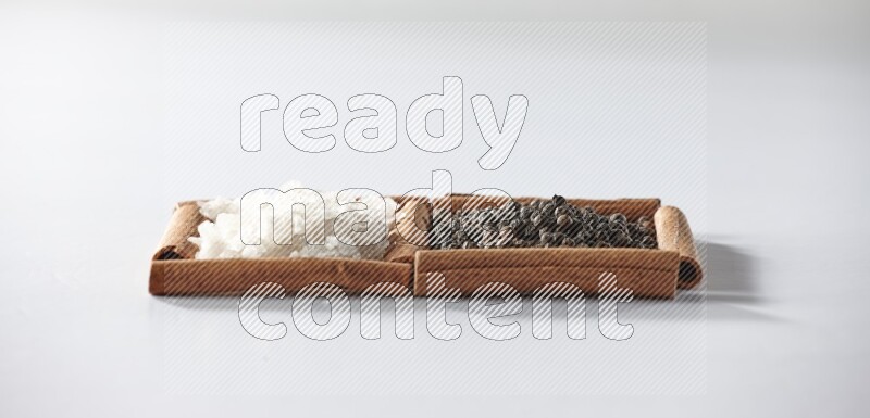 2 squares of cinnamon sticks full of black pepper and white salt on white flooring