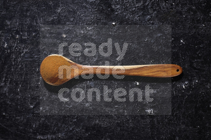 A wooden ladle full of ground paprika powder on black background