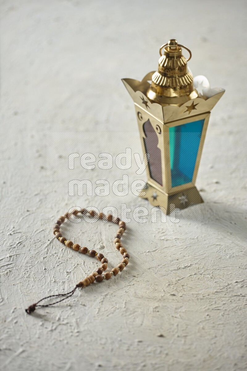 A golden lantern with different drinks, dates, nuts, prayer beads and quran on textured white background