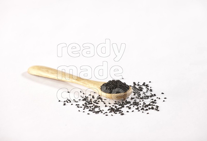 A wooden spoon full of black seeds on a white flooring