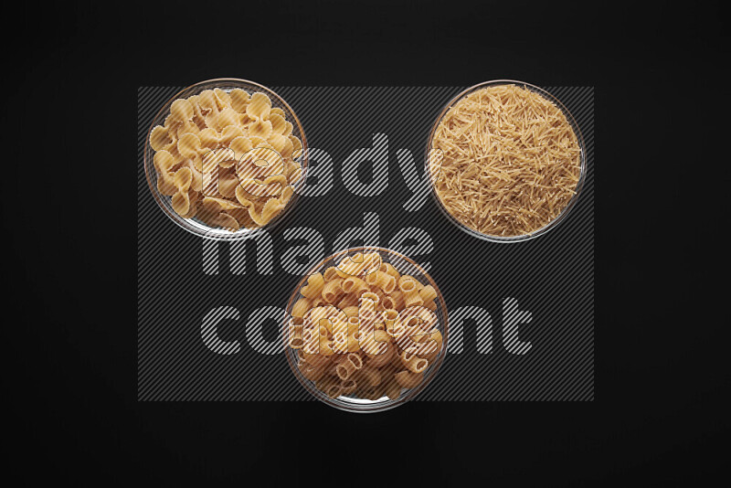 Different pasta types in glass bowls on black background